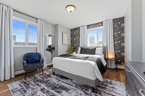 A bedroom with a bed, a chair, a nightstand, and a dresser.