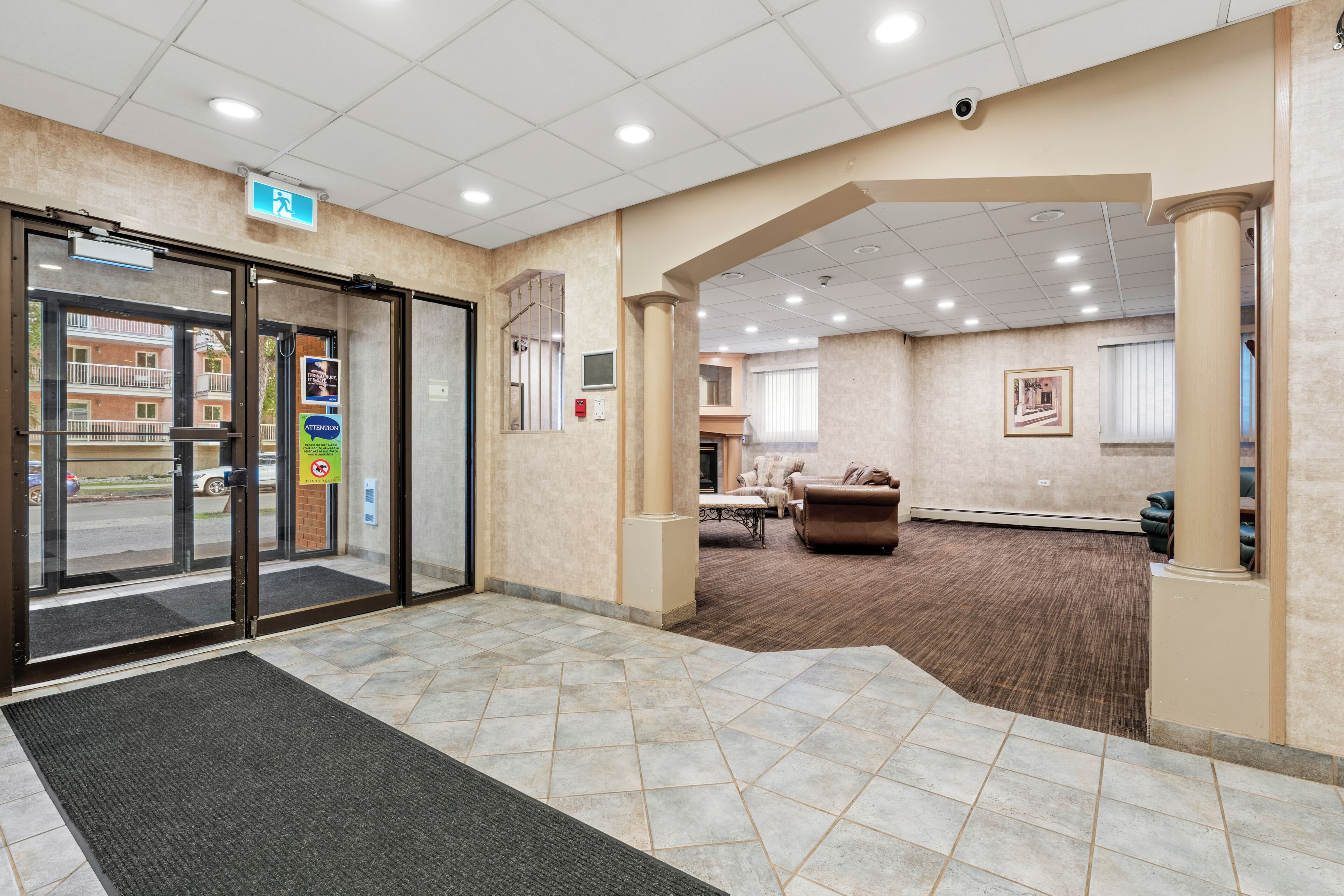 A hotel lobby with a reception desk, a waiting area with a sofa, and a view of the street through the entrance.