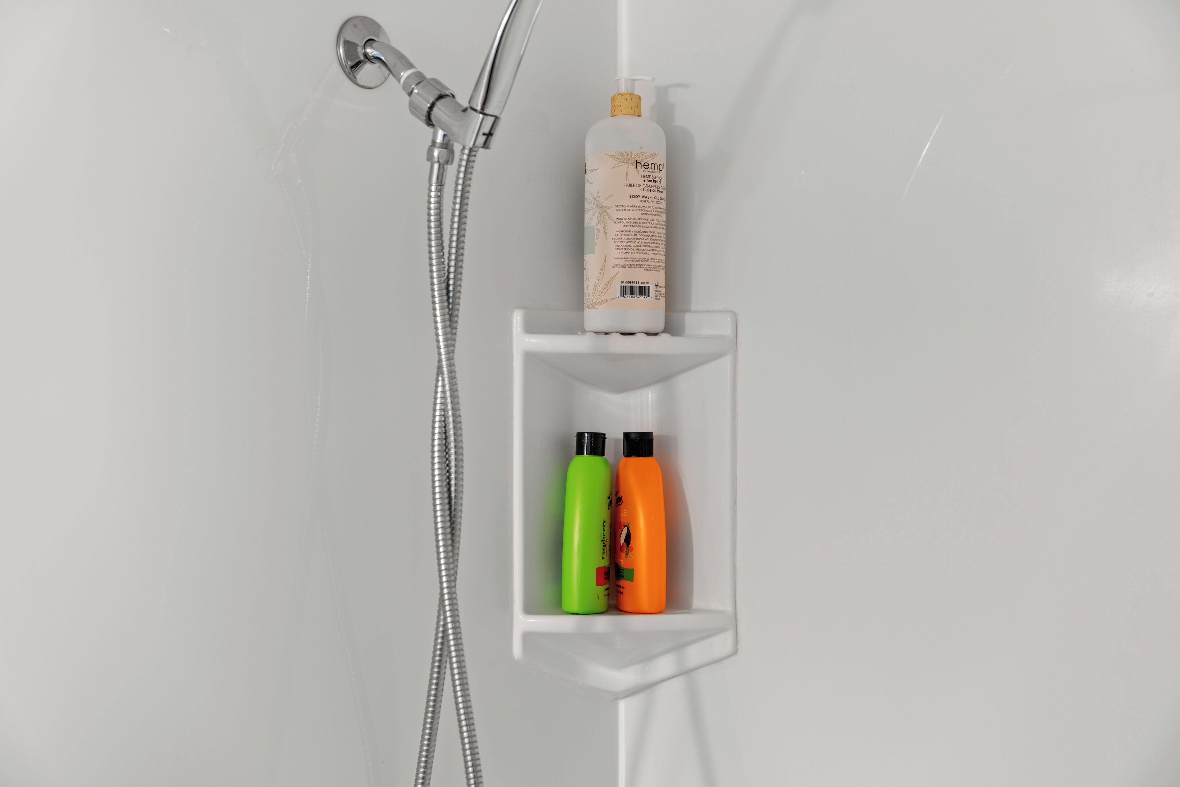 A bathroom with a shower, a white sink, and a shelf with three bottles of shampoo and conditioner.