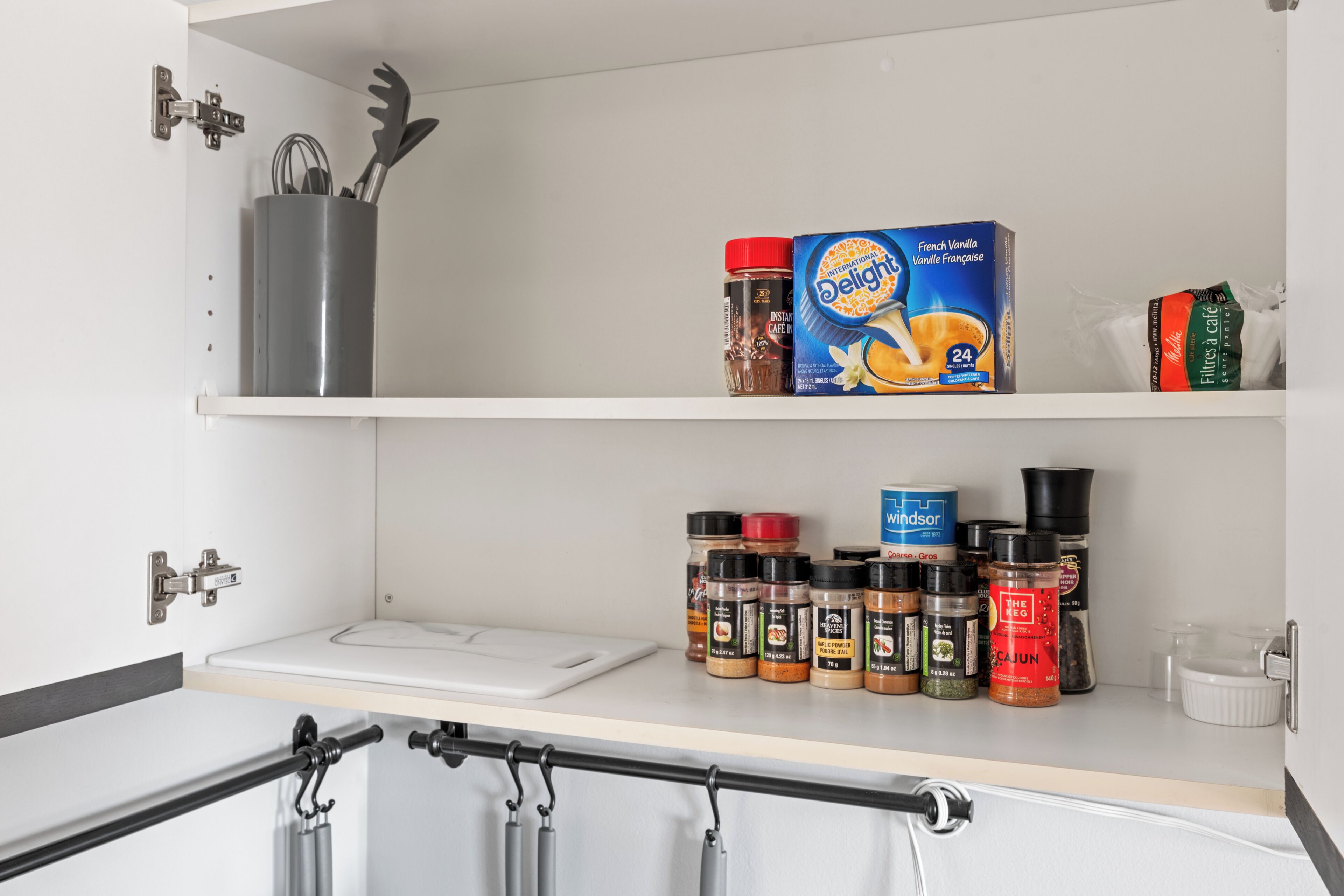 A kitchen with a white countertop, a coffee maker, a box of French vanilla instant coffee, and various spice containers.