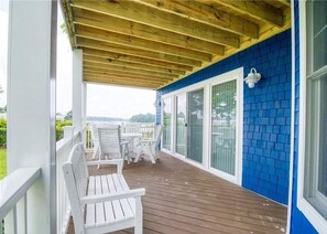 Eine überdachte Terrasse mit weißen Stühlen und einem Tisch, blauen Wänden und Blick aufs Meer.