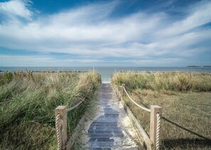 Um caminho que leva a uma praia, com corrimãos de madeira e encostas gramadas.