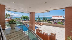Un balcón de hotel con piscina, mobiliario exterior y vistas al océano.