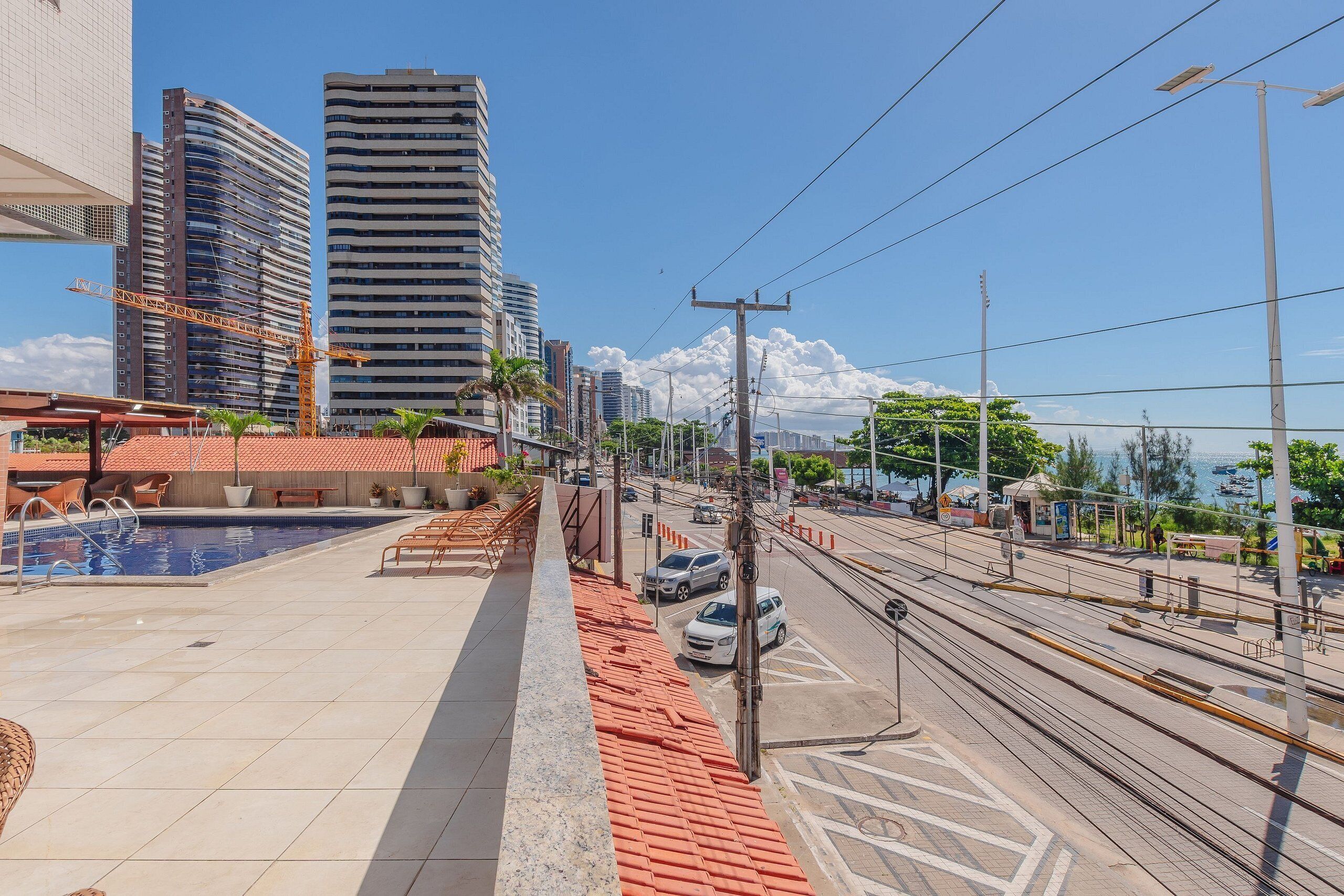 A rooftop pool area with a view of tall buildings, a tram line, and a clear sky.