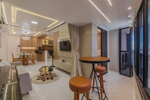 Ein modernes Wohnzimmer mit einer Couch, einem Esstisch und einer Küchenzeile mit Fernseher.