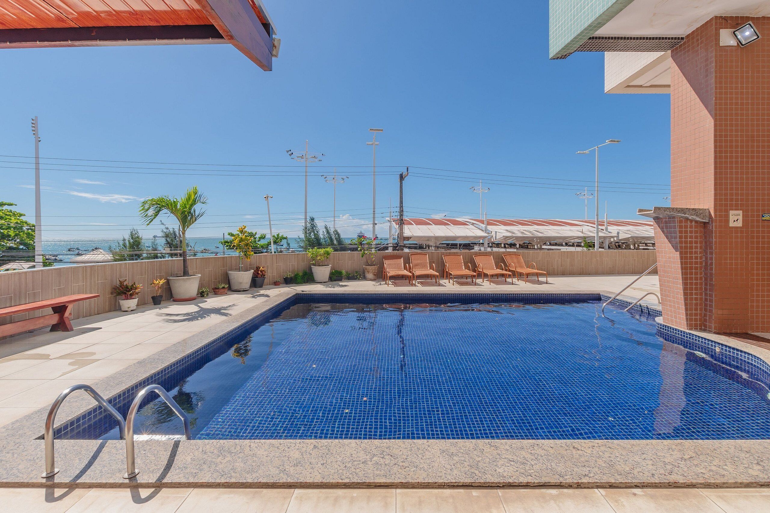 Una piscina con borde de azulejos, un banco y sillas de descanso.