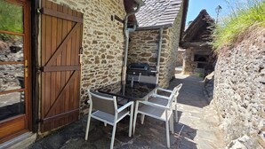 Ein Steinhäuschen mit einer Holztür, einem Tisch mit Stühlen und einem Grill vor der Tür.