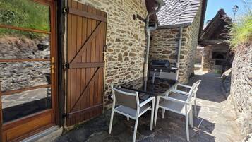 Een stenen gebouw met een houten deur, een tafel met stoelen en een barbecue buiten.