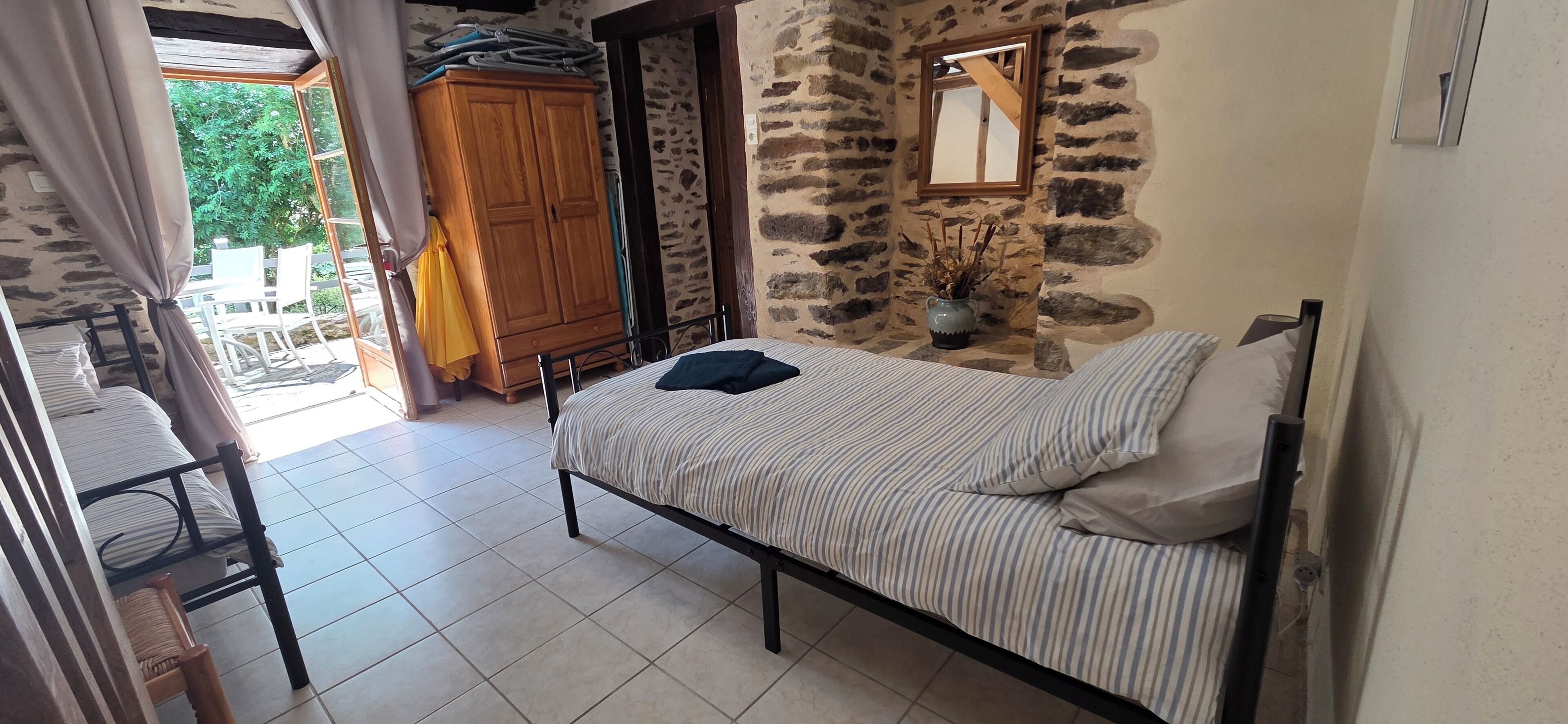 Une chambre à coucher avec un lit, une armoire, un miroir et un mur en pierre.