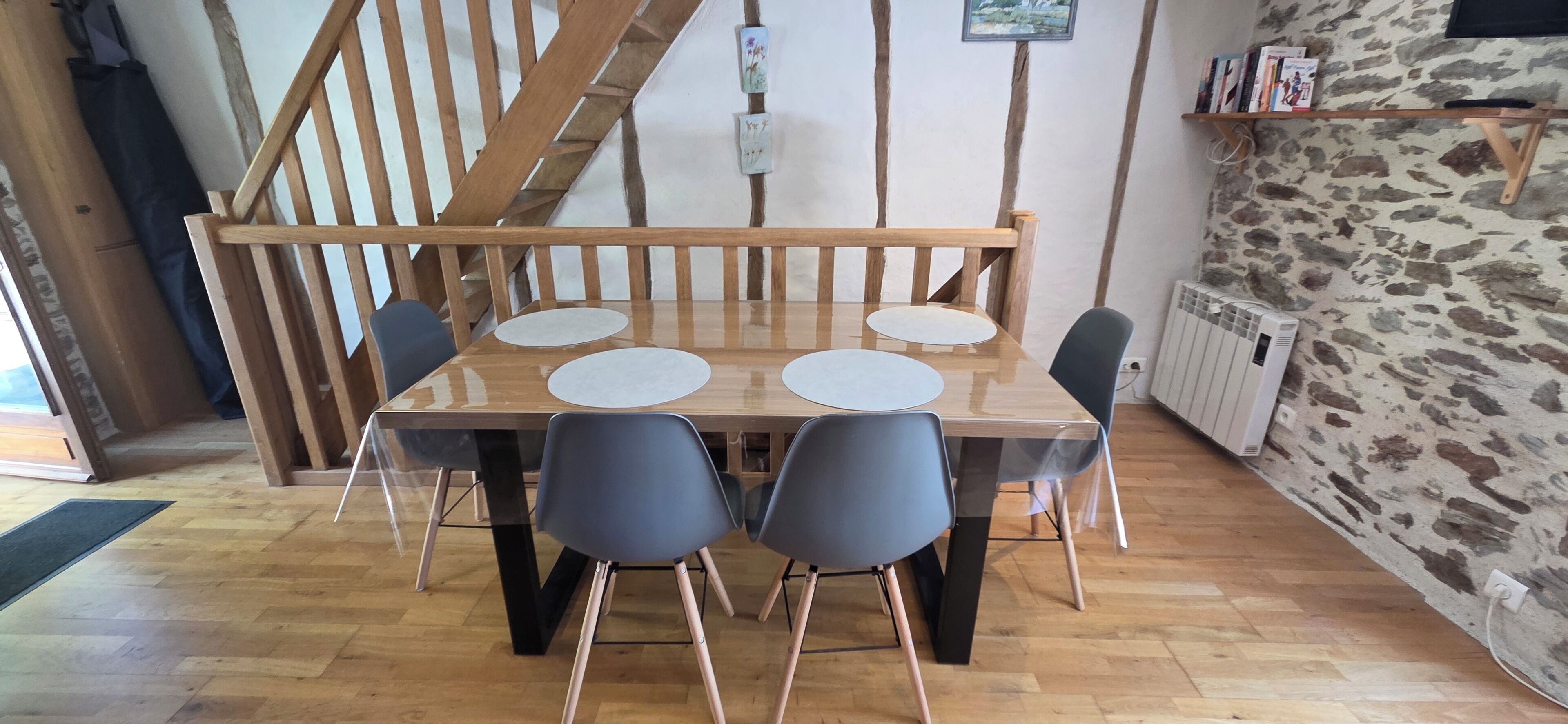 Een eetgedeelte met een houten tafel, vier stoelen, een trap en een stenen muur.