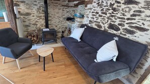 Ein gemütliches Zimmer mit Steinwand, Holzboden, einer Couch, einem Sessel und einem kleinen Tisch.