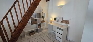 Un escalier avec des rampes en bois, un bureau blanc avec des tiroirs, des étagères avec des paniers, un globe terrestre, une lampe et un luminaire fixé au mur.