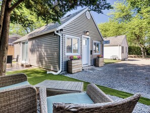 A single-story cabin with a front porch, a small deck, and a gravel driveway.