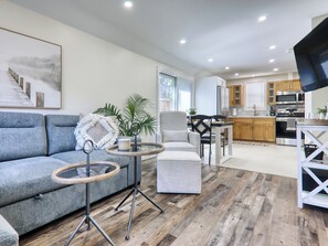 A modern living room with a grey sofa, a round coffee table, and a dining area with a white table and chairs.