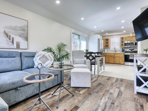 A modern living room with a grey sofa, a round coffee table, and a dining area with a white table and chairs.