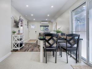 A modern kitchen with a dining area, white walls, and a large window.