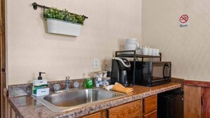 Eine kleine Küche mit Spüle, Arbeitsplatte, Holzschränken, einer Mikrowelle und einer Kaffeemaschine.