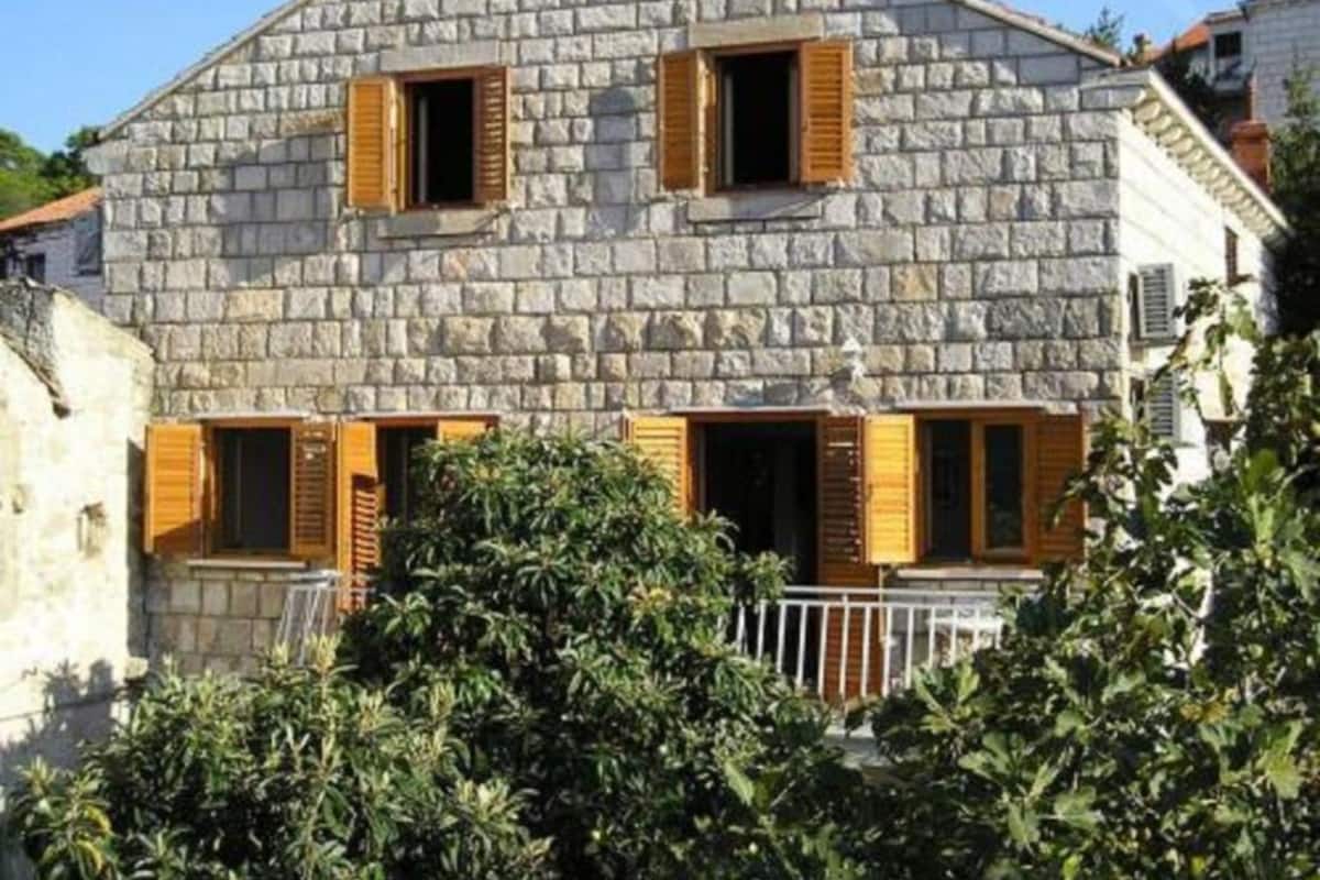 Un edificio de piedra con contraventanas de madera, un balcón y una barandilla blanca.