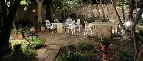 Eine Terrasse im Freien mit Steinböden, weißen Plastikstühlen und einem Tisch.