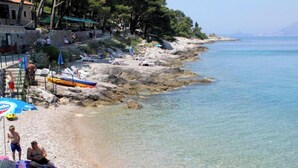 Ein felsiger Strand mit klarem Wasser, Sonnenschirmen und einigen Personen.