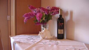 Ein Tisch mit einer blumigen Tischdecke, einer Vase mit rosa Blumen und einer Weinflasche.