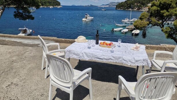 Ein Tisch mit einer Flasche, einem Hut und Obst auf einer Tischdecke, mit Blick auf einen Yachthafen und Boote.