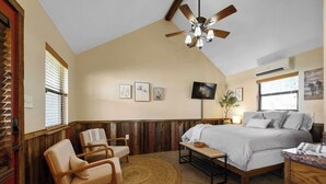 A bedroom with a bed, two chairs, a TV, and a ceiling fan. - The Fantail at Nicole Creek Cabins (Waco)