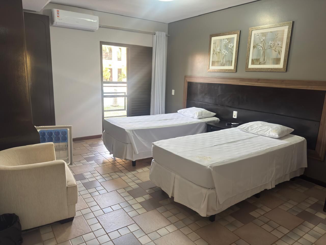 Une chambre d’hôtel avec deux lits, une chaise, un appareil de climatisation et une fenêtre avec des rideaux.