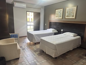 A hotel room with two beds, a chair, an air conditioning unit, and a window with curtains. - GoldMen Business Sorriso (Sorriso)