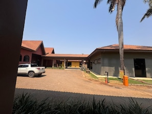 A building with a red-tiled roof, a white SUV parked in front, and a palm tree. - GoldMen Business Sorriso (Sorriso)
