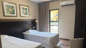Habitación de hotel con dos camas, cabecera, ventana con cortinas, unidad de aire acondicionado y refrigerador.