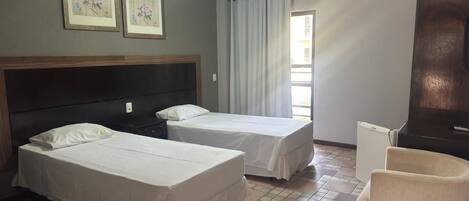 A hotel room with two beds, a chair, an air conditioning unit, and a window with curtains.