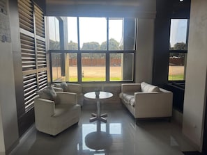 A room with two sofas, a round table, and large windows with a view of a fenced outdoor area.