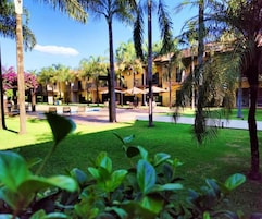 Un resort con área de piscina, palmeras y un edificio con balcones.