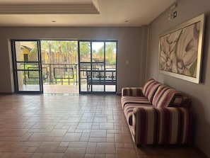 A spacious room with a tiled floor, a striped sofa, a large window with a view of palm trees, and a painting on the wall. - GoldMen Business Sorriso (Sorriso)