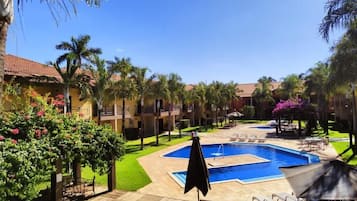 Zona de piscina en un resort, con una piscina central, sillas de descanso y palmeras.