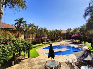 A resort pool area with a central swimming pool, lounge chairs, and palm trees.