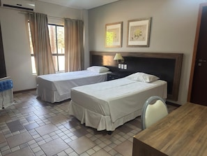 A hotel room with two beds, a wooden table, a chair, a nightstand, a lamp, and a window with curtains. - GoldMen Business Sorriso (Sorriso)