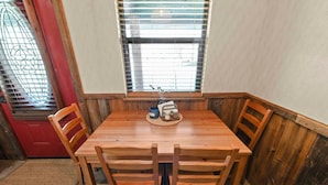 Un coin repas avec une table et des chaises en bois, une fenêtre avec des stores et une porte rouge.