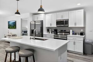 A modern kitchen with white cabinetry, stainless steel appliances, and a central island with stools. - Charming Home in Port Charlotte – Sunshine Getaway (Port Charlotte)