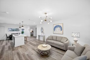 A modern living room with a sofa, a coffee table, and a dining area with a kitchen island. - Charming Home in Port Charlotte – Sunshine Getaway (Port Charlotte)