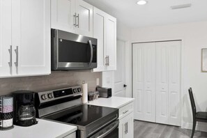 A modern kitchen with white cabinetry, a stainless steel microwave, an oven, and a coffee maker. - Charming Home in Port Charlotte – Sunshine Getaway (Port Charlotte)