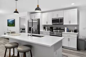 A modern kitchen with white cabinets, stainless steel appliances, a large island with stools, and pendant lighting. - Charming Home in Port Charlotte – Sunshine Getaway (Port Charlotte)