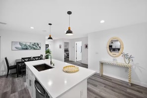 A modern kitchen with a central island, pendant lighting, and a decorative mirror. - Charming Home in Port Charlotte – Sunshine Getaway (Port Charlotte)