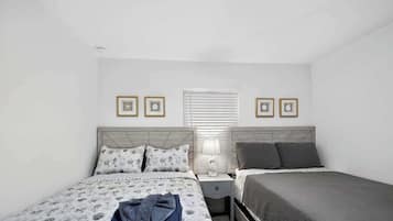 A bedroom with two beds, a nightstand, a lamp, and framed pictures on the wall.