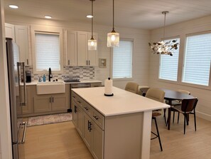 A modern kitchen with a central island, pendant lighting, and a dining area with chairs.