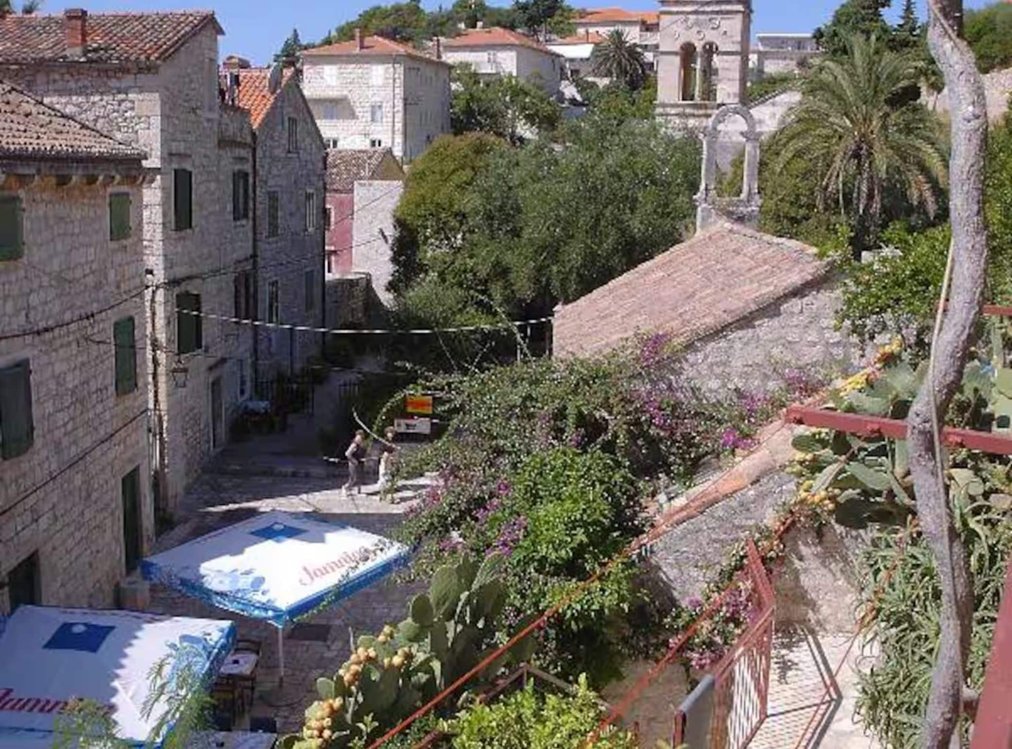 A narrow street with stone buildings, a small bridge, and a tree-lined path.