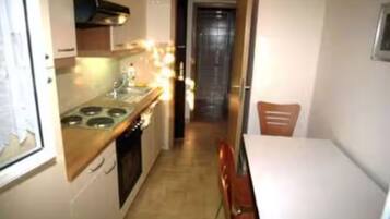 A narrow kitchen with a stove, oven, and a dining table with chairs.