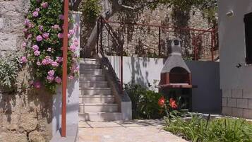 A stone staircase leading to a building with a chimney, surrounded by flowering plants and a metal fence.