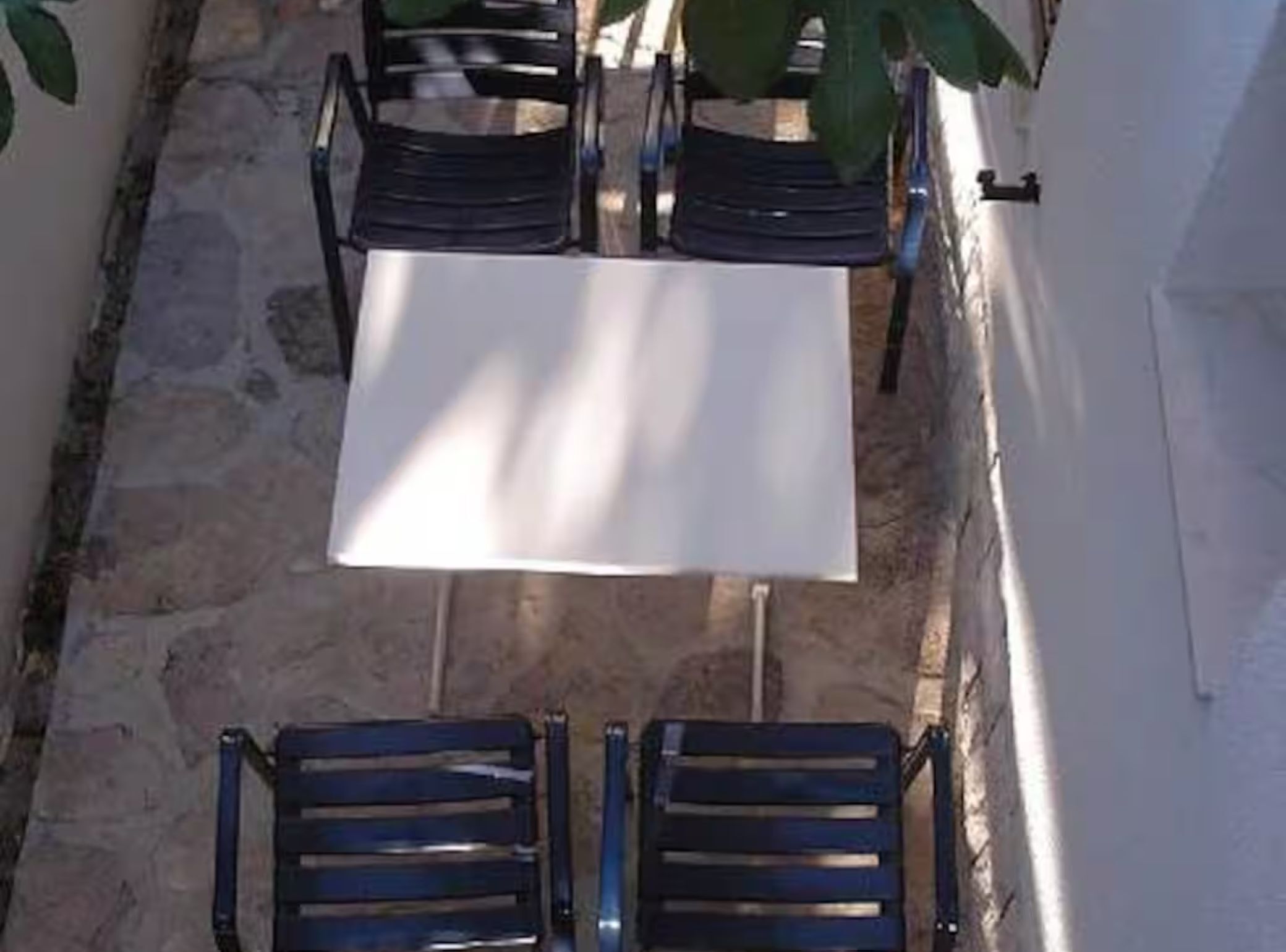 A patio with a table and four chairs, surrounded by stone walls and a white building.
